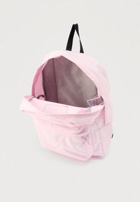 Sac à dos rose clair avec poche avant zippée, boucle noire pour suspendre et compartiment principal ouvert montrant une doublure intérieure claire à motifs.