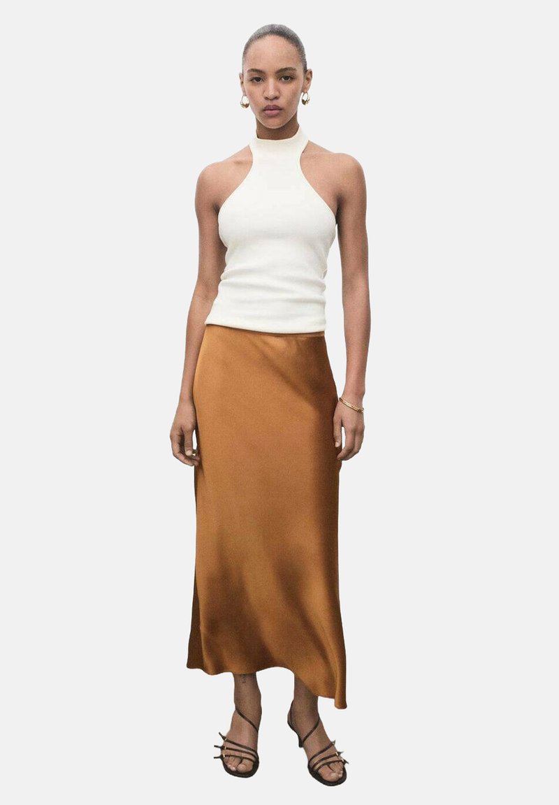 Bílý halter top se přiléhavým střihem, v kombinaci s volnou hnědou saténovou midi sukni. Sandály na tenkých páscích v černé barvě. Jednoduché zlaté náušnice doplňují celkový vzhled.