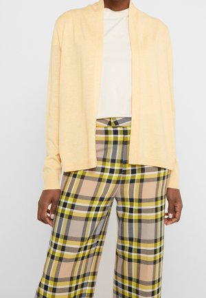 Lys gul cardigan med åben front og ribstrikkede manchetter, parret med brede, ternede bukser i beige, grøn, grå og hvid.