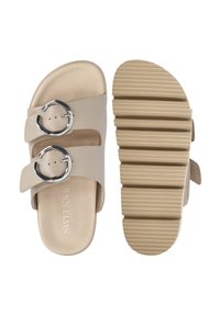 Beige sandals with two wide straps and silver circular buckles, featuring a textured rubber sole with ridges for grip and cushioning.