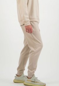Beige, taillierter Sweatshirt und passende Jogginghosen aus weichem Stoff, mit gerippten Bündchen und einem dezenten Logo auf der Hose. Sneakers in Hellgrün.
