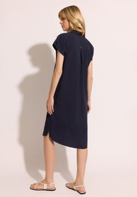 Granatowa sukienka z krótkimi rękawami, bocznymi rozporkami i detalem w postaci guzika na ramieniu. Miękka tkanina, luźny krój, długość midi.