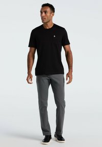 Zwarte t-shirt met korte mouwen en een borstzak. Gecombineerd met grijze broek en zwarte sneakers. Eenvoudig ontwerp, geen zichtbare patronen.