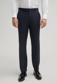 Pantaloni da uomo in navy su misura con tessuto liscio, taglio dritto e fronte piatto. Abbinati a scarpe eleganti nere.