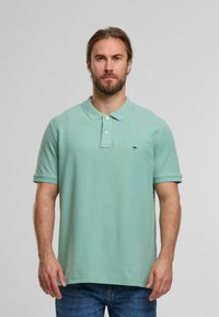 Ljusgrön polo t-shirt med krage och tre knappar, tillverkad av bomull. Har korta ärmar och en liten marinblå logotyp på vänster bröst.