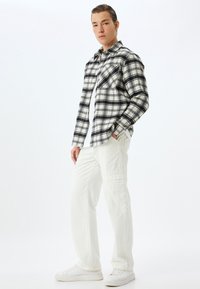 Zwart-wit geruit flanellen shirt met voorzakken, gecombineerd met witte cargobroek en witte sneakers. Soepele stof, casual stijl.