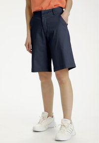 Pantaloni corti blu navy dal design semplice, realizzati in tessuto leggero, con due tasche laterali e orlo dritto. Abbinati a sneakers bianche.