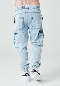 Pantalones cargo de mezclilla azul claro con cintura elástica, bolsillos laterales y puños ajustados, combinados con zapatillas blancas con acentos negros.