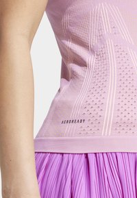 Lichtpaarse mouwloze top met een textuurpatroon, featuring perforaties en lichte strepen. Logo "AEROREADY" in het zwart op de taille.