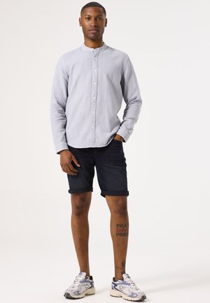 Lichtblauw overhemd met een mandarinnekraag, gecombineerd met donkere denim shorts. Model draagt grijs-witte sportschoenen.