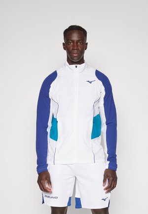 Mizuno Sportjacke in Weiß mit blauen und türkisfarbenen Akzenten, ausgestattet mit einem hohen Kragen, einem Reißverschluss vorne und einem strukturierten Design. Weiße Shorts ergänzen das Outfit.