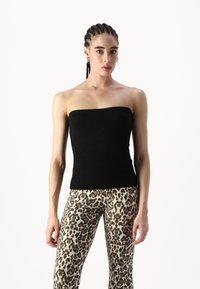 Melnā strapless blūze ar ribotu struktūru un piegulīgu dizainu, apvienota ar bēšām leopardu raksta legingām, kurām ir tumši punkti.