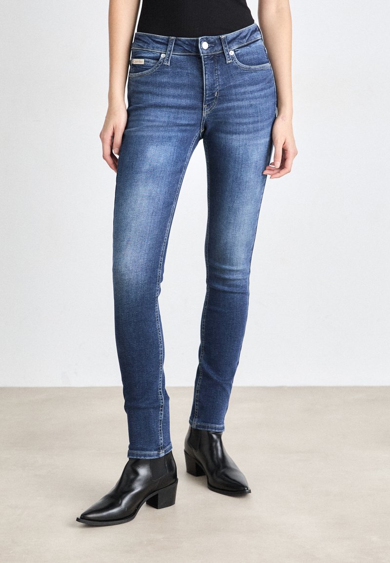 Λεπτά μπλε τζιν παντελόνια με φθαρμένο πλύσιμο, που διαθέτουν κλασικό σχέδιο πέντε τσεπών και μέση μεσαίου ύψους, σε συνδυασμό με μαύρες μποτες μέχρι τον αστράγαλο.