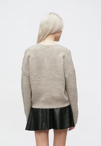 Beige kötött pulóver laza szabással, lelógó vállakkal és bordás szegéllyel. Fekete bőr miniszoknyával párosítva.