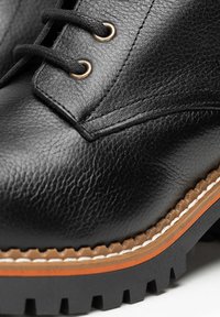 Scarpa in pelle nera con tomaia testurizzata, occhielli in bronzo, lacci neri e suola esterna a contrasto marrone e bianca con motivo a rilievo.