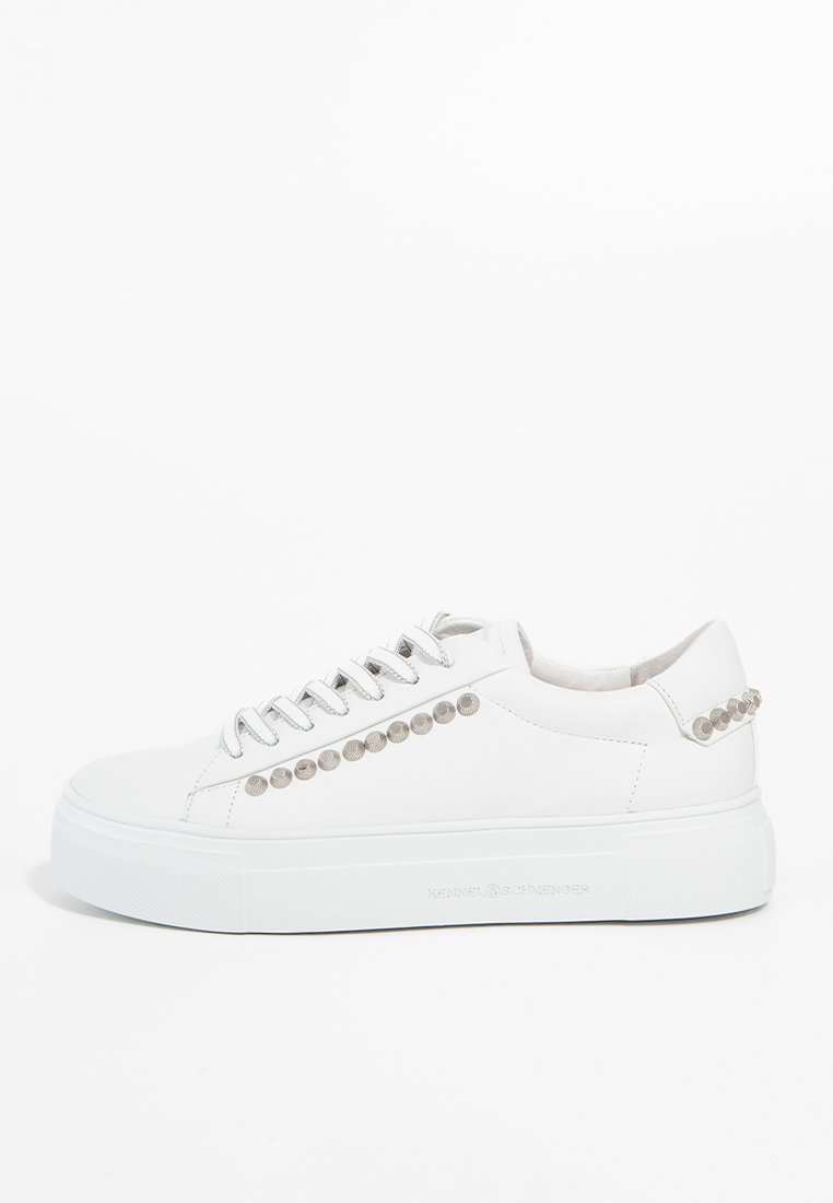 Weiße Low-Top-Sneaker mit silbernen Nieten an der Seite und Ferse, dicker Sohle und weißen Schnürsenkeln auf einem schlichten weißen Hintergrund.