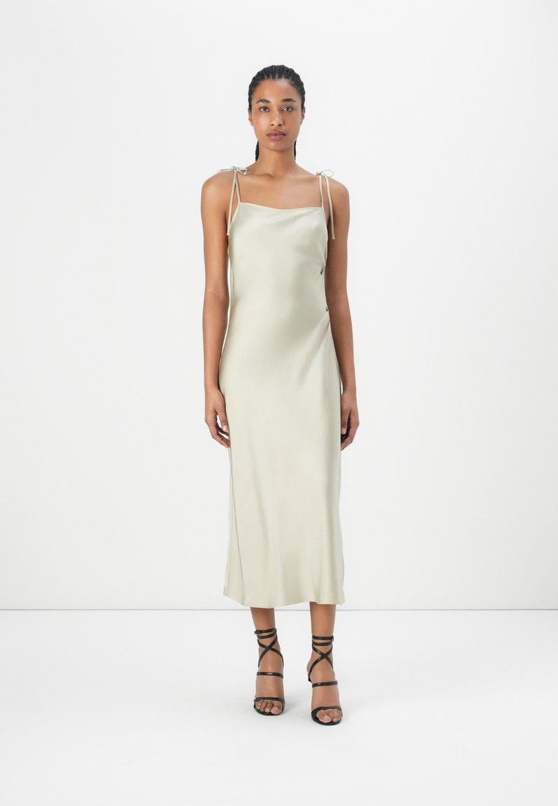 Satin-Midi-Kleid in Hellgrün mit verstellbaren Bindeträgern, geradeem Ausschnitt und taillierter Silhouette. Schwarze Riemchen-Heels runden den Look ab.