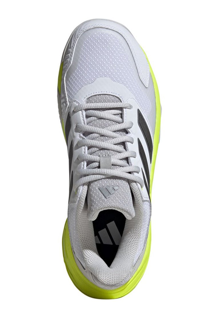 Zapatilla deportiva blanca con parte superior de malla, acentos negros y suela exterior amarilla brillante. Presenta cordones y una puntera texturizada.