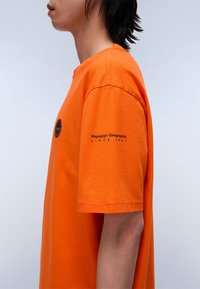 Orange bomuld t-shirt med en afslappet pasform, korte ærmer og rund hals; har et logo på brystet og ærmet.