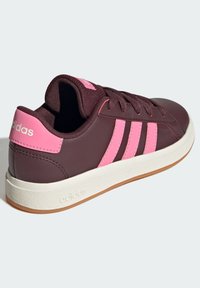 Zapatilla burdeos con acentos en rosa y tres franjas, que cuenta con una suela de goma texturizada y un cuello acolchado para mayor comodidad.