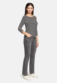 Schwarz-weiß gestreiftes Langarmhemd kombiniert mit grauen geraden Jeans, getragen mit weißen Sneakers, was einen lässigen Look zeigt.