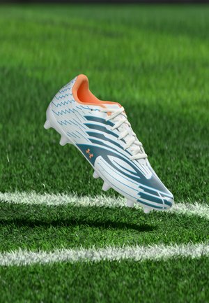 Weiß-blauer Fußballschuh mit orangefarbenen Innenschnürsenkeln auf grünem Rasen nahe weißen Linienmarkierungen.