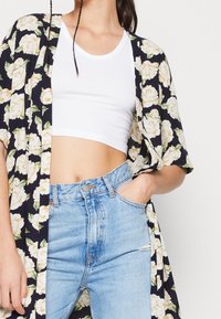 Květinové kimono s námořnickým pozadím, zdobené krémovými růžemi a zelenými listy. Doplněné bílým zkráceným topem a světle modrými džíny s vysokým pasem.