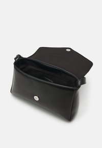 Czarna prostokątna skórzana kopertówka z magnetycznym zapięciem na zatrzask, otwierana klapka odsłania czarne materiałowe wnętrze oraz metkę z nazwą marki.