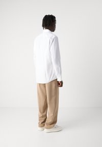 Hvid langærmet skjorte med knap-ned krave, parret med beige brede bukser og hvide sneakers, set fra ryggen.