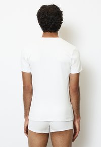 Weißes Kurzarm-T-Shirt mit Rundhalsausschnitt aus geripptem Baumwollstoff. Figurbetontes Design, kombiniert mit passenden weißen Shorts.
