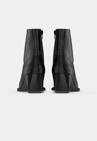 Bottines en cuir noir avec un design épuré, dotées d'une fermeture éclair, d'un talon carré et d'une texture lisse. Bout arrondi et détails de couture minimalistes.