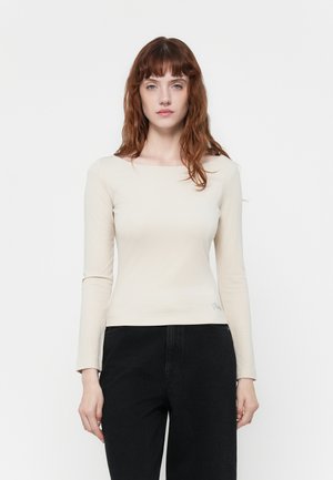Top de manga larga color beige claro con escote cuadrado, hecho de una tela suave, con un corte ajustado y un sutil detalle del logo en el dobladillo.
