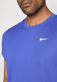 Nike πορτοκαλί αθλητική μπλούζα κοντομάνικη με στρογγυλή λαιμόκοψη και ένα μικρό λευκό λογότυπο στο στήθος, φτιαγμένη από έναν λείο, αναπνεύσιμο ύφασμα.