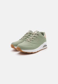 Green athletic shoes with a textured upper, lace-up design, white midsole, and tan rubber outsole. Features air cushioning in the heel.