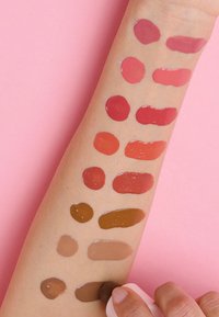 Campioni di colore per labbra mostrati su un braccio con tonalità di pelle, con varie sfumature dal rosa al marrone in forme circolari e ovali, con una consistenza lucida.