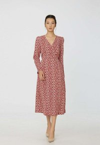 Robe maxi florale rouge avec des manches longues, un décolleté en V et une taille cintrée. Présente des motifs floraux blancs sur un tissu doux et léger.