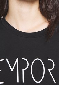 Černé bavlněné tričko s kulatým výstřihem a výrazným bílým nápisem "TEMPOR". Textura vypadá hladce a látka je lehká.