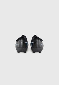 Une paire de crampons de soccer Nike Mercurial noirs vue de l'arrière avec une surface texturée et des crampons sous les semelles sur un fond uni.