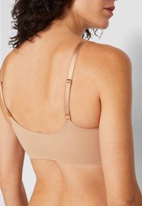 Beige seamless bra with thin adjustable straps, featuring back hook closures and a smooth, matte texture on a neutral background.