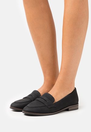 Musta loafersi, joissa on sileä mokkanahka pinta, tasapohja ja koristeellinen ommel. Pyöreä kärki ja matala korko.