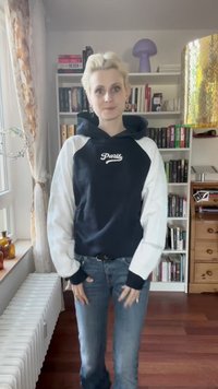 Jūrinės ir baltos spalvos sportinė striukė su „Paryžius“ grafika, raglan tipo rankovėmis ir tekstūruotu audiniu. Suderinta su šviesiai mėlynomis džinsais.