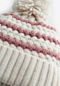 Gebreide beanie met crème en zachte roze strepen, voorzien van een textuurpatroon en een fluffy pompon bovenop. Geribbelde manchetrand.