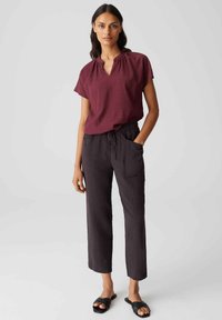 Blusa bordeaux a maniche corte con scollatura rotonda, abbinata a pantaloni neri larghi con vita regolabile e tasche frontali. Sandali neri.