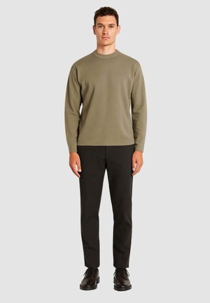 Maglione verde oliva a maniche lunghe, colletto a girocollo, abbinato a pantaloni scuri e scarpe nere. Texture liscia, design minimalista, senza motivi.