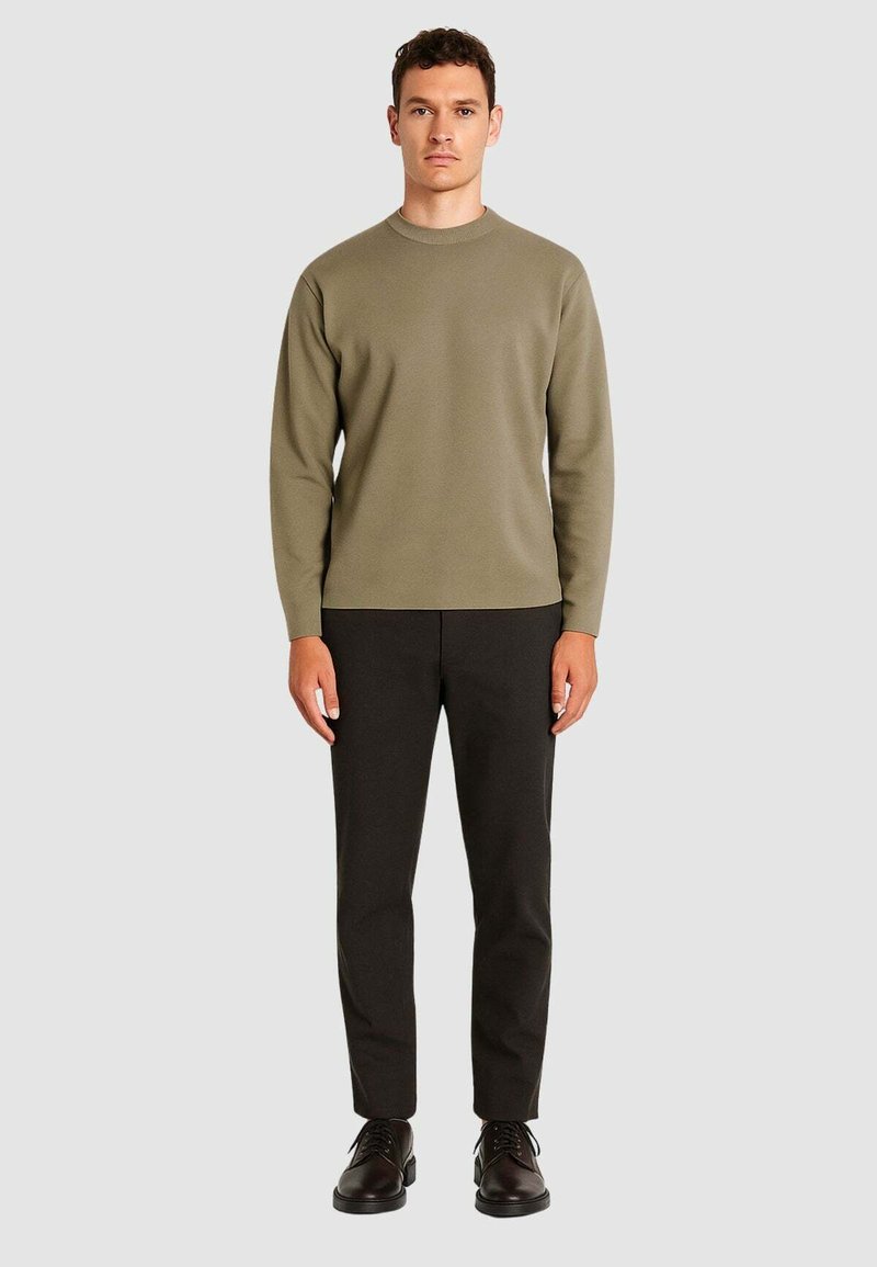 Maglione verde oliva a maniche lunghe, colletto a girocollo, abbinato a pantaloni scuri e scarpe nere. Texture liscia, design minimalista, senza motivi.