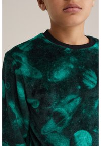 Șrăcăminte din fleece verde și negru cu o suprafață texturată, având un design cu model circular. Guler ribbat negru.