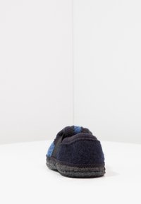 Blaue und marineblaue Wollslipper zum Hineinschlüpfen mit einer strukturierten Oberseite, kontrastierenden schwarzen Seitenelementen und einer dicken grauen Gummisohle.