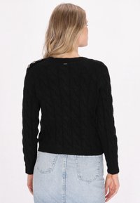 Maglione nero lavorato a maglia con motivo a treccia, maniche lunghe e bottoni sulle spalle. Realizzato in tessuto testurizzato, design aderente. Vista posteriore mostrata.