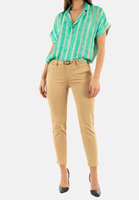Camisa de rayas turquesa de manga corta combinada con pantalones ajustados beige y zapatos de tacón negro. El cinturón es de un color contrastante.