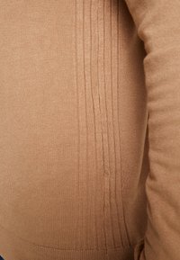 Lys brun strikket sweater med ribbestruktur langs siden, tætsiddende design og glat stof med en subtil glans.
